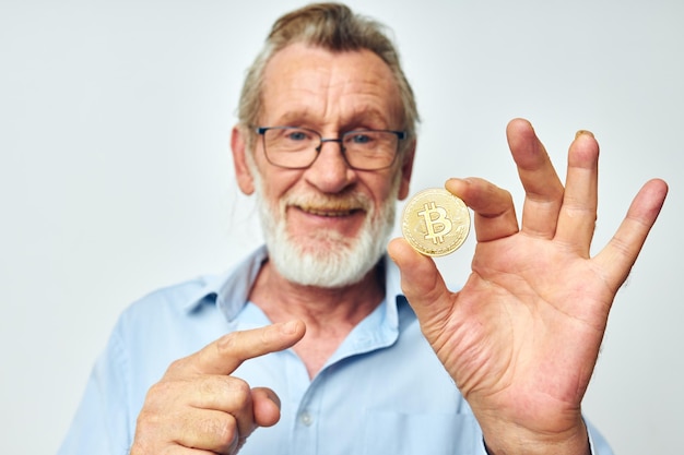 Senior homme aux cheveux gris finance des pièces d'or bitcoin posant sur fond clair