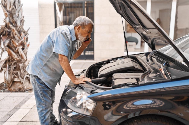 Photo senior homme aux cheveux gris parlant avec une assurance pour un problème de moteur de voiture dans la rue