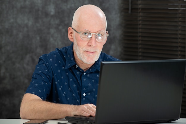 Senior homme avec une barbe et une chemise bleue au bureau à l&#39;aide d&#39;un ordinateur portable