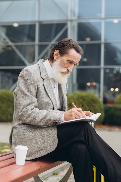 Senior homme à barbe grise avec valise de transport et plan de la ville est assis et écrire des notes dans le cahier le long de l'aéroport