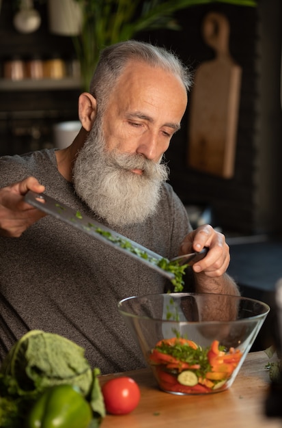 Senior homme barbu préparer une salade saine et savoureuse dans la cuisine.