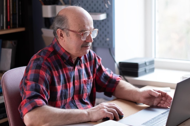 Senior homme caucasien avec des lunettes avec un ordinateur portable à la maison à la recherche sur Internet