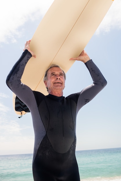 Senior homme en combinaison en cours d'exécution avec planche de surf sur la tête