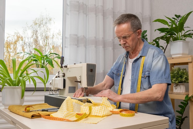 Senior homme couturière assis et coud sur machine à coudre en studio Concept d'usine