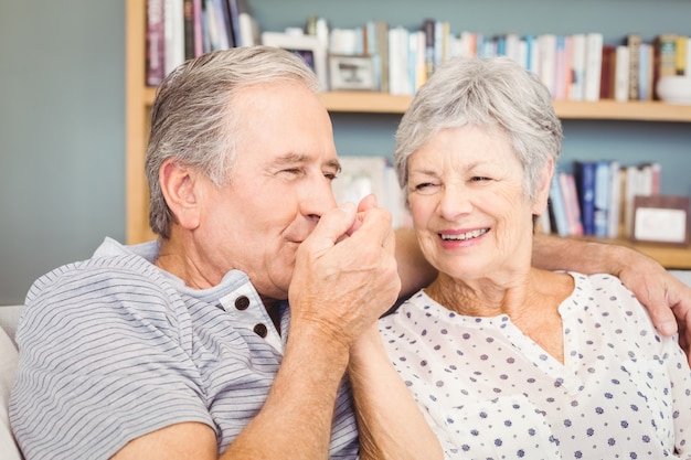 Senior homme embrassant la main de sa femme assis à la maison