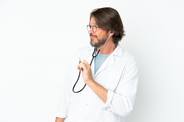 Senior homme hollandais isolé sur fond blanc portant une robe de médecin et avec stéthoscope