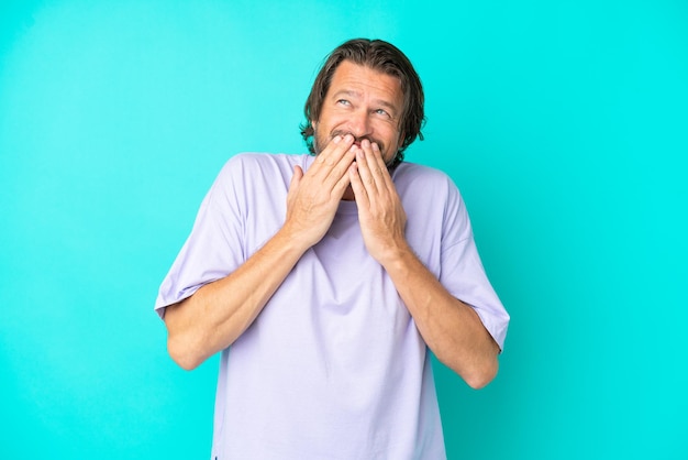 Senior homme hollandais isolé sur fond bleu heureux et souriant couvrant la bouche avec les mains