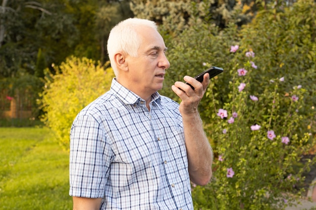 Senior homme mature à l'aide de téléphone mobile avec recherche vocale dans green park, technologies modernes