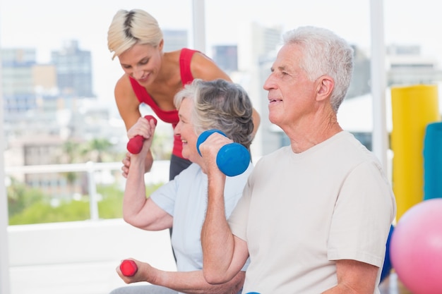 Senior homme soulevant des haltères pendant que l&#39;entraîneur aidant une femme au gymnase