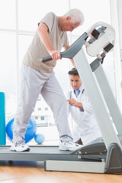 Senior homme sur tapis roulant avec un thérapeute accroupi