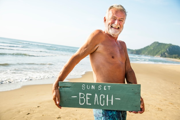 Photo senior homme tenant un panneau à la plage
