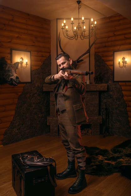 Senior hunter en vêtements de chasse traditionnels rétro vise le fusil de chasse antique contre le vieux coffre.