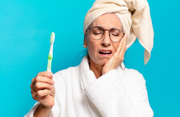 Photo senior jolie femme après la douche en peignoir et avec une brosse à dents