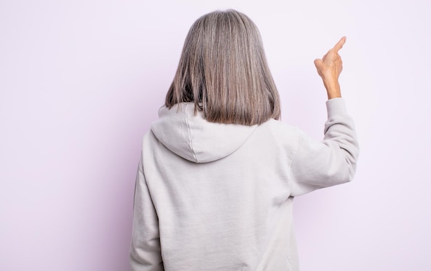 Senior jolie femme debout et pointant vers l'objet sur la vue arrière de l'espace de copie