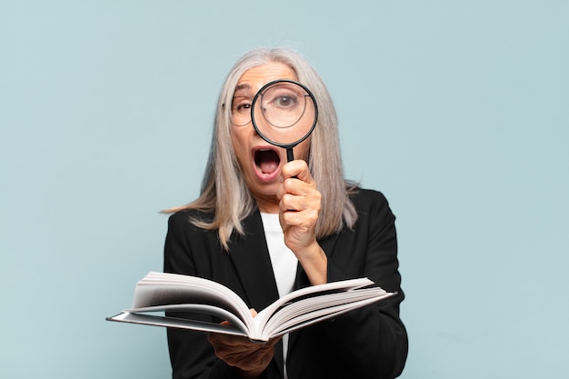 Senior jolie femme avec un livre et une loupe. concept de recherche