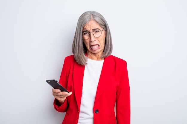 Senior jolie femme se sentant dégoûtée et irritée et langue dehors .. concept d'entreprise et de téléphone