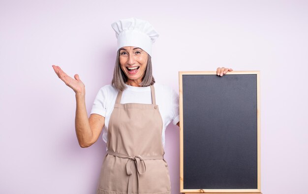 Senior jolie femme se sentant heureuse et étonnée de quelque chose d'incroyable. concept de chef et tableau noir