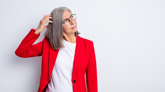 Senior jolie femme souriant joyeusement et rêvassant ou doutant. notion de femme d'affaires