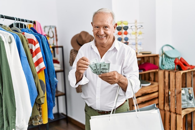 Senior man client souriant confiant comptant des dollars au magasin de vêtements
