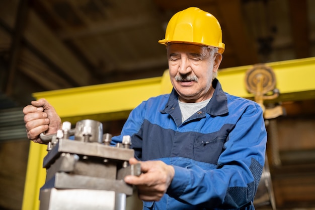 Senior man in casque et contrôle uniforme de l'état du générateur de fer de grande machine industrielle