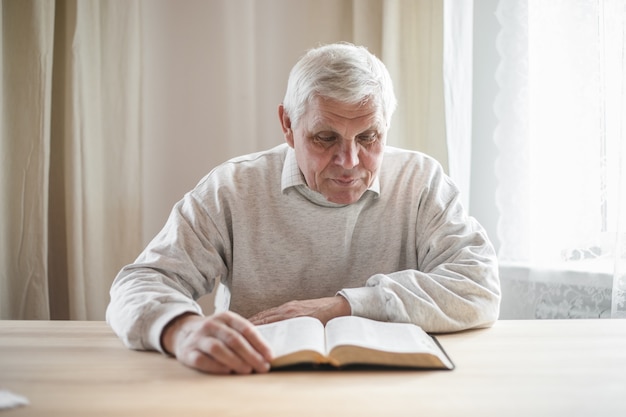 Senior man priant, lisant une vieille Bible dans ses mains.