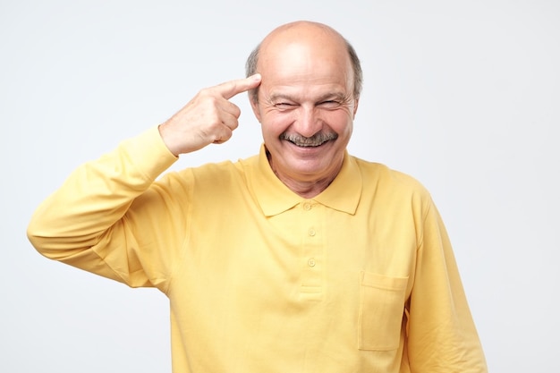 Senior man smiling pointant vers la tête avec un doigt bonne idée ou pensée