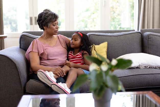 Senior mixed race woman appréciant son temps à la maison, assis sur un canapé, embrassant sa petite-fille, la regardant