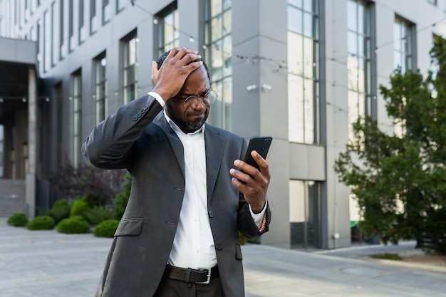 Senior patron afro-américain mature lisant de mauvaises nouvelles au téléphone homme d'affaires en costume d'affaires à l'extérieur