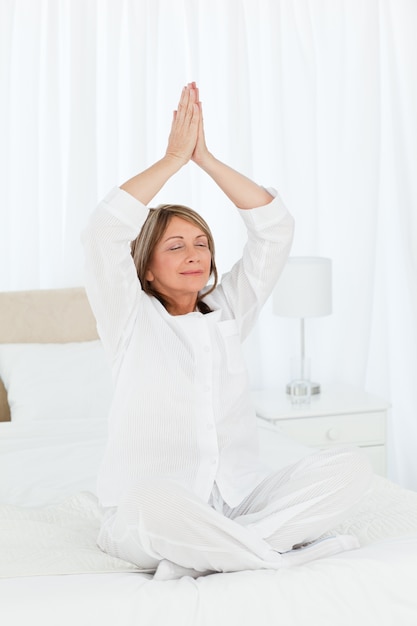 Senior pratiquant le yoga sur son lit
