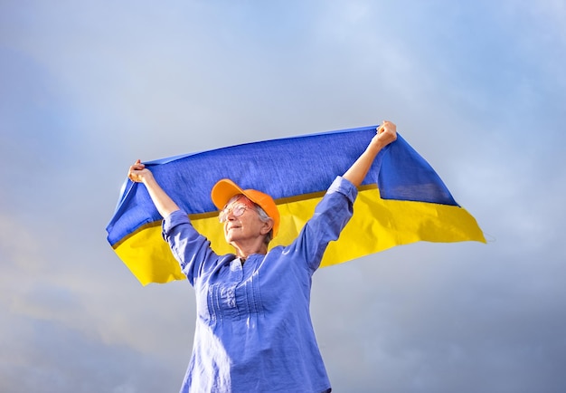 Photo senior whitehaired woman wearing eyeglasses debout à l'extérieur dans le pays agitant le drapeau ukrainien à la recherche de liberté sentiment de liberté pas de combats d'arrêt de guerre, nous voulons la paix