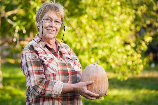 Senior woman dans une chemise à carreaux tient une citrouille dans le jardin.