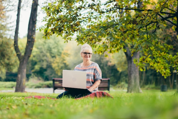 Senior woman détente dans le parc avec un ordinateur portable