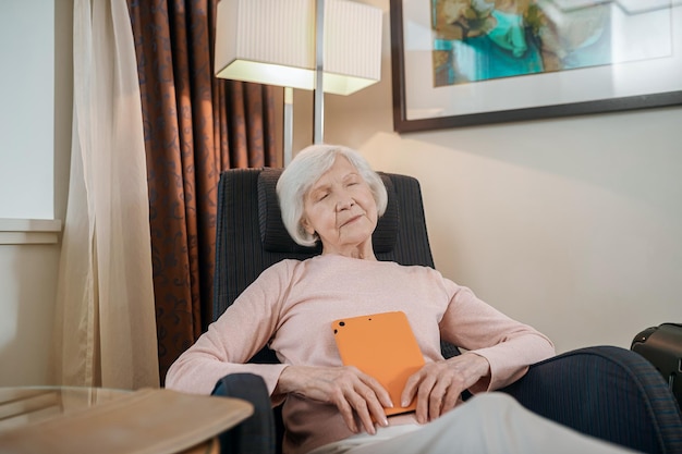 A senior woman in pink blouse avec une tablette assise dans un fauteuil