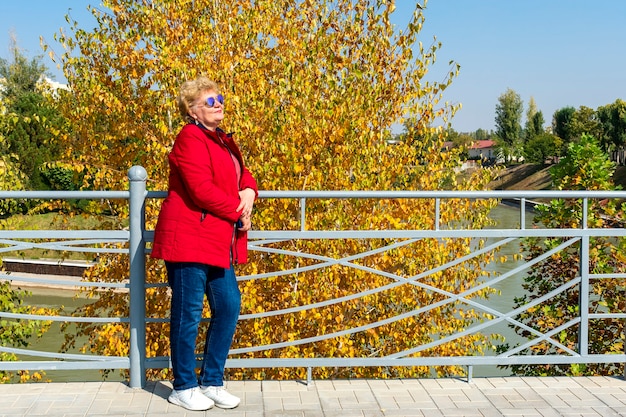 Photo senior woman in red jacket marchant et relaxant dans la nature dans le parc. temps d'automne