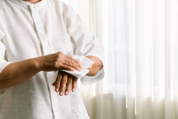 Senior woman nettoyant ses mains avec du papier de soie doux blanc. isolé sur un tableau blanc