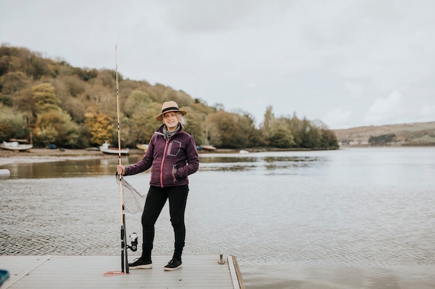 Senior woman posing avec une canne à pêche au bord du lac