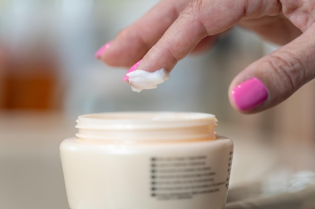 Senior woman's hand picking cream avec son doigt pour les soins personnels de la peau