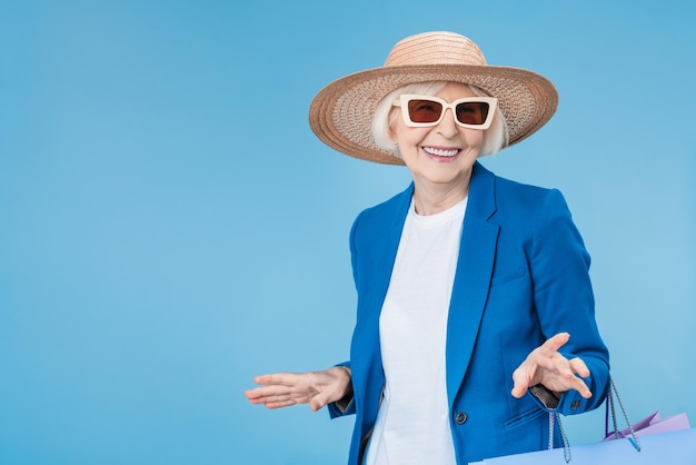 Senior woman shopper portant des lunettes de soleil et un chapeau avec des sacs isolés sur fond bleu