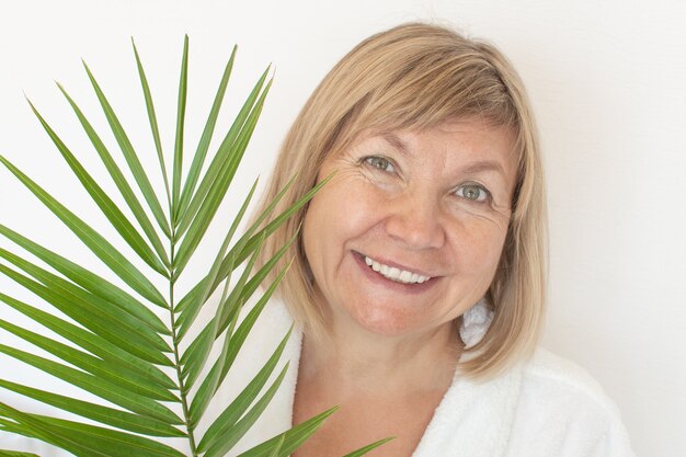 Senior woman smiling concept anti-âge avec feuille de palmier. Visage de femme mature après un traitement au spa. Vieillesse dans la joie, clinique de chirurgie plastique, mignonne grand-mère, cosmétologie, nouveau senior, retraité, personnes d'âge mûr