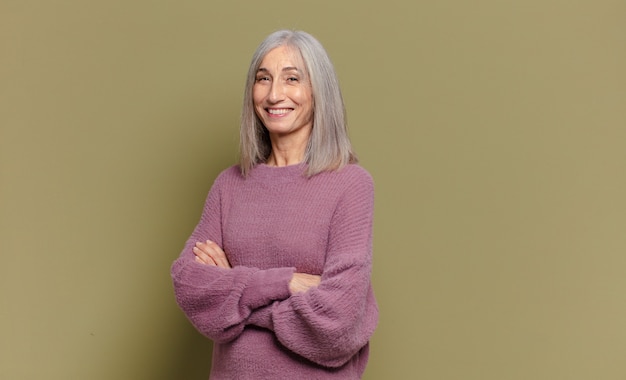 Senior woman smiling to camera avec les bras croisés et une expression heureuse, confiante, satisfaite, vue latérale