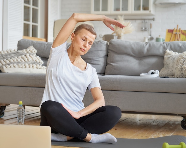 Senior woman stretching hand formation en ligne avec ordinateur portable dans le salon exercice pour le bien-être