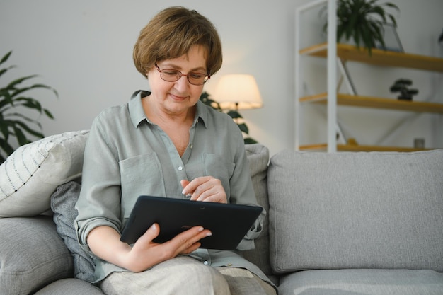 Senior woman using digital tablet in living room at home