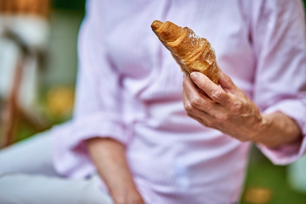 Senior woman va prendre le petit déjeuner avec un croissant