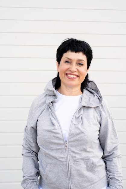 Senior woman waring veste grise debout à l'extérieur sur un mur solide gris