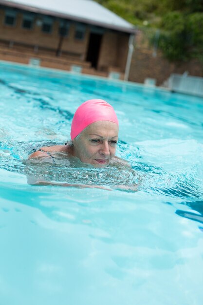 Senior woman wearing pink cap en nageant dans la piscine