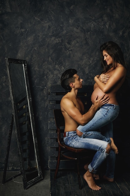 Sensuel jeune couple en attente d'un bébé. L'homme et sa femme enceinte posant à l'intérieur.