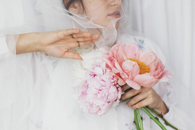 Sensuelle belle femme sous un tissu de tulle doux tenant un bouquet de pivoines dans les mains Image tendre