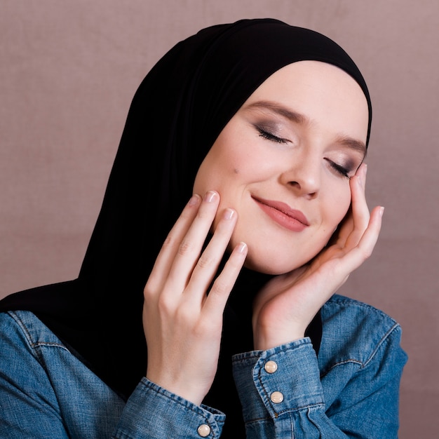 Photo sensuelle femme arabe touchant ses joues contre une surface colorée