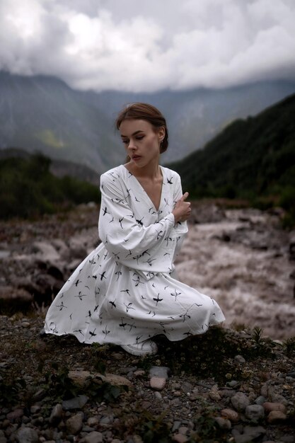 Sensuelle fille élégante aux cheveux bruns dans une robe blanche se trouve dans les montagnes