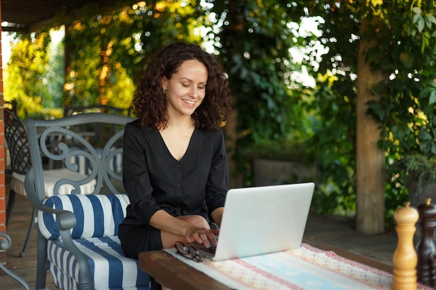 Sensuelle jeune femme travaillant sur un ordinateur portable assis sur la terrasse en regardant la caméra